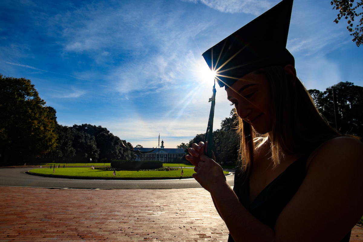 A graduate cast in shadow pauses in front of an image of the "front" of the school, in the bachground sits Hoggard hall and in front of it is a statue of  a Seahawk that sits in a roundabout